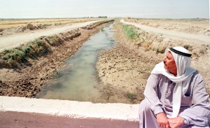 IRAQI FARMER SITS BESIDE A NEARLY DRY RIVER.